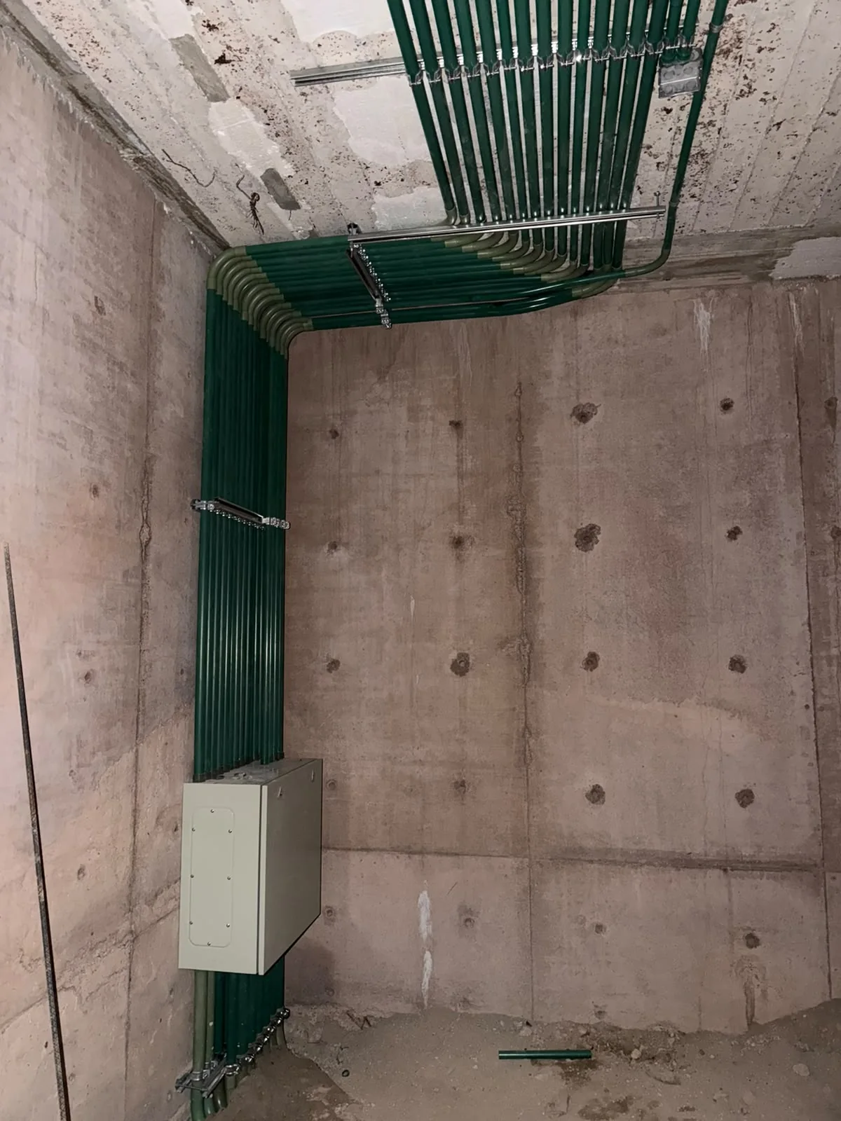 Canalizaciones verdes alineadas en el techo y muro, conectadas con un gabinete metálico.
