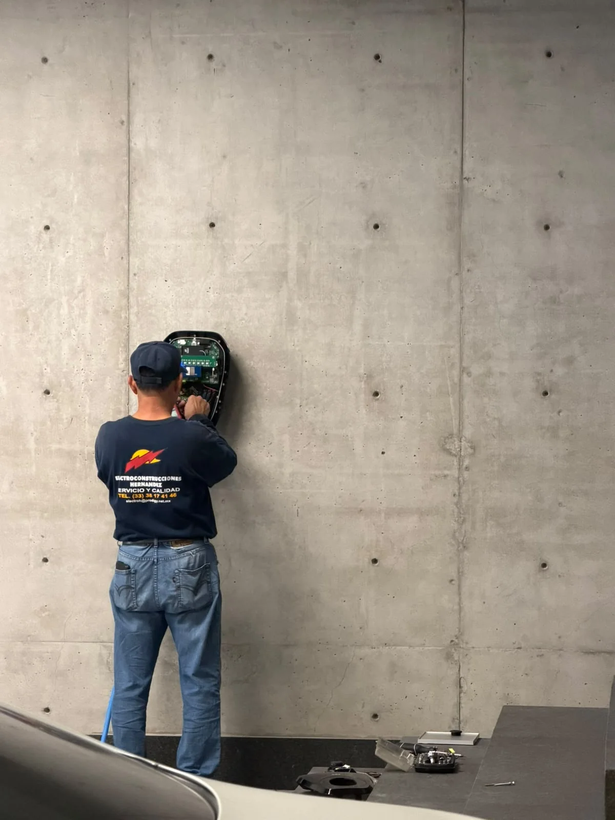 Técnico con uniforme de ElectroH realizando trabajos dentro de un equipo fijado a un muro de concreto.