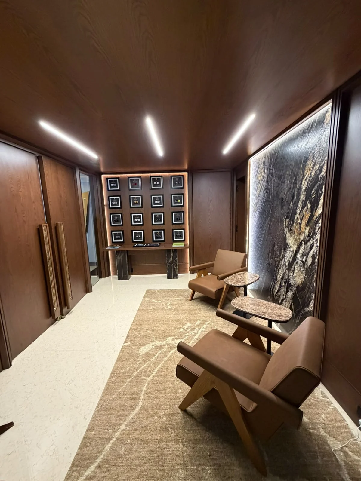 Sala con asientos, revestimientos de madera y líneas de luz en el techo.